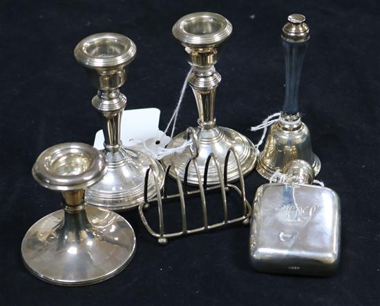 A small silver hip flask, a pair of silver dwarf candlesticks, another candlestick, a small toast rack and a silver table bell